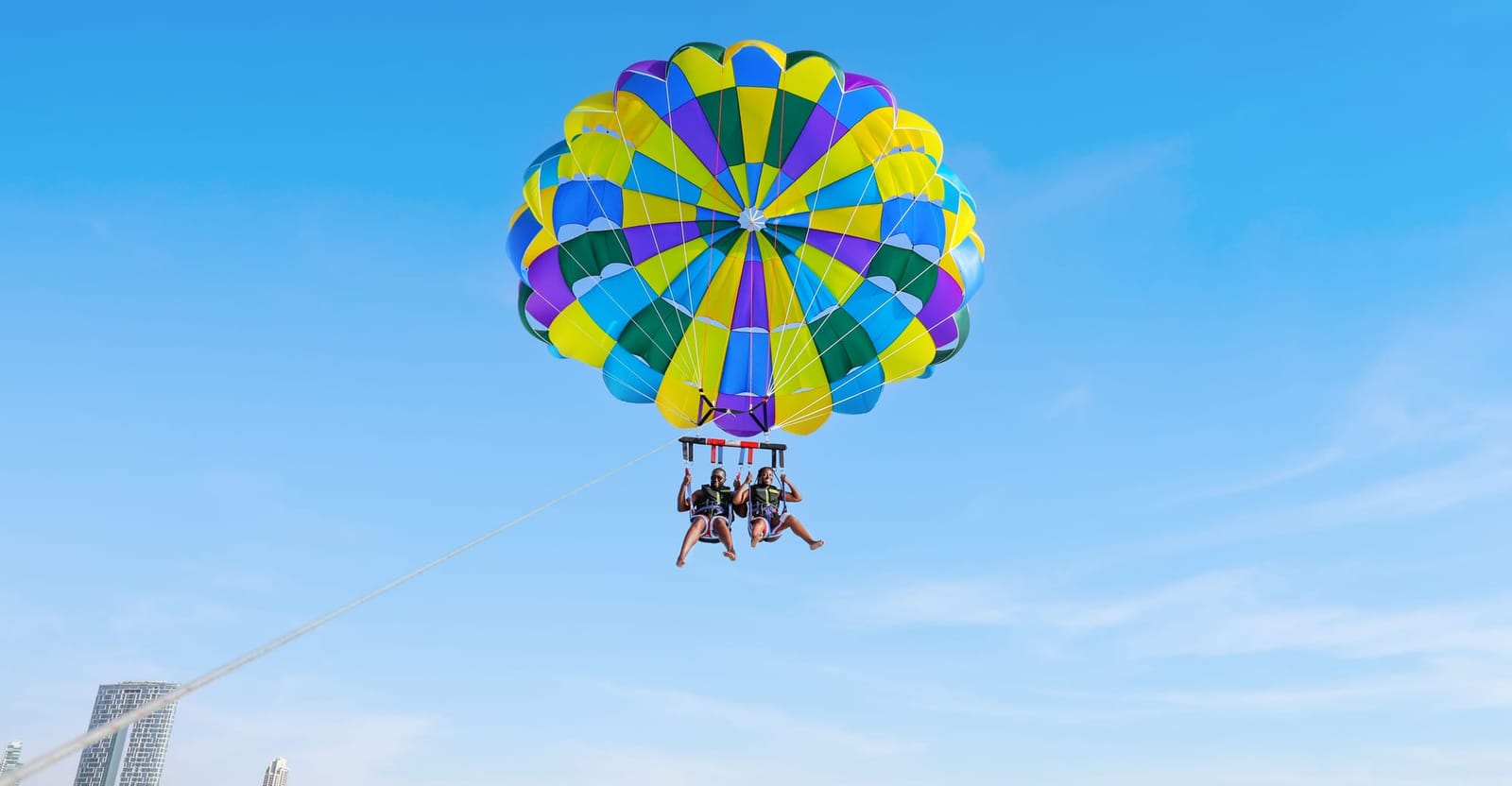 Zwei Personen bei einem Tandem-Parasailing-Flug unter einem bunten Schirm am klaren Himmel über Dubai
